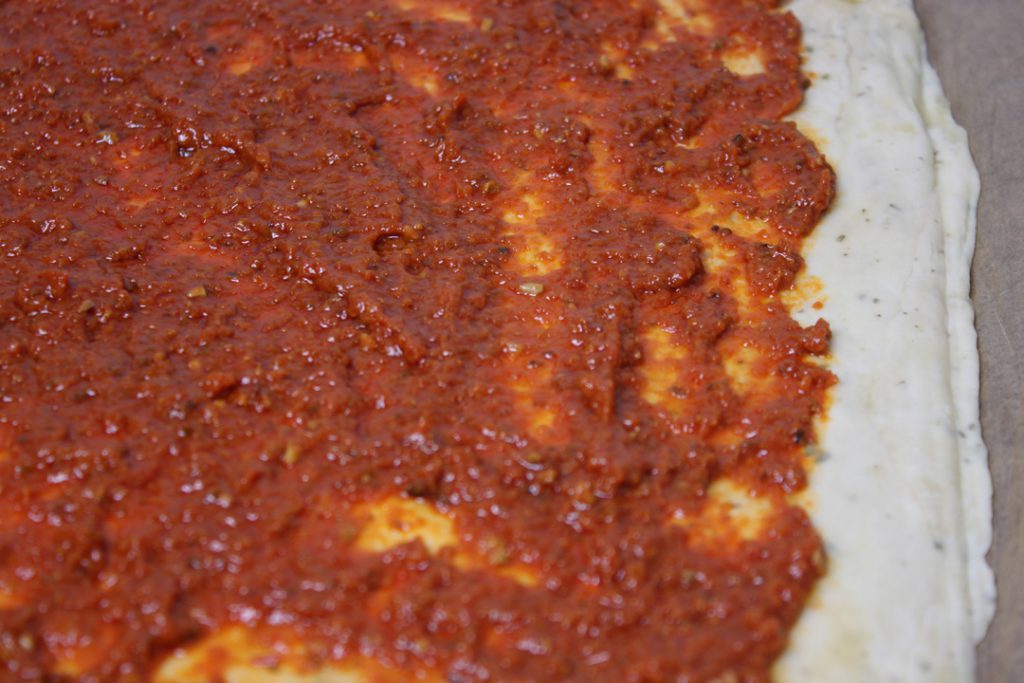 Für die Mangold Pizza den ausgerollten Teig mit dem Pesto bestreichen